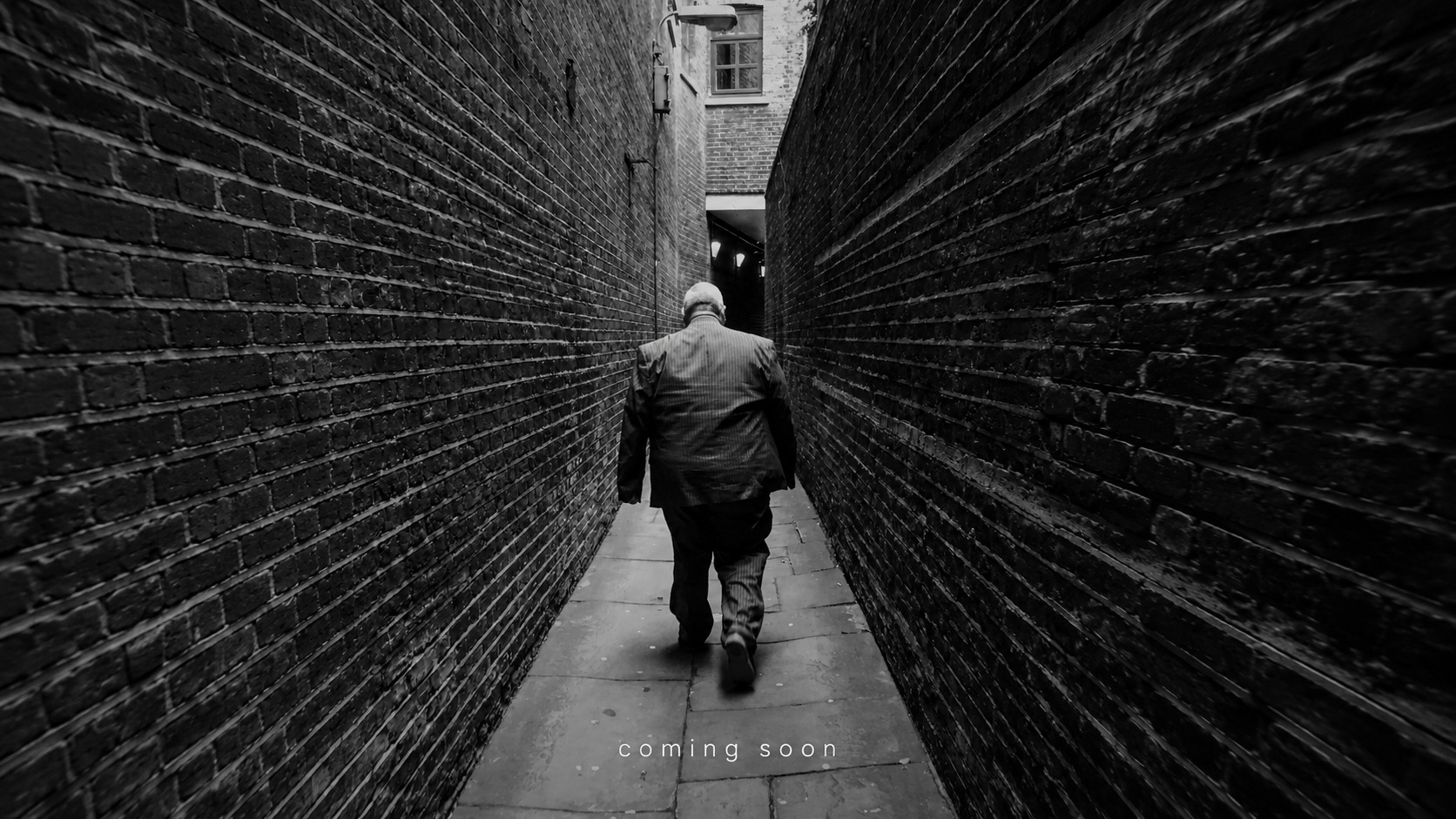 Black and white photograph of a man walking down a narrow alley with the words coming soon.